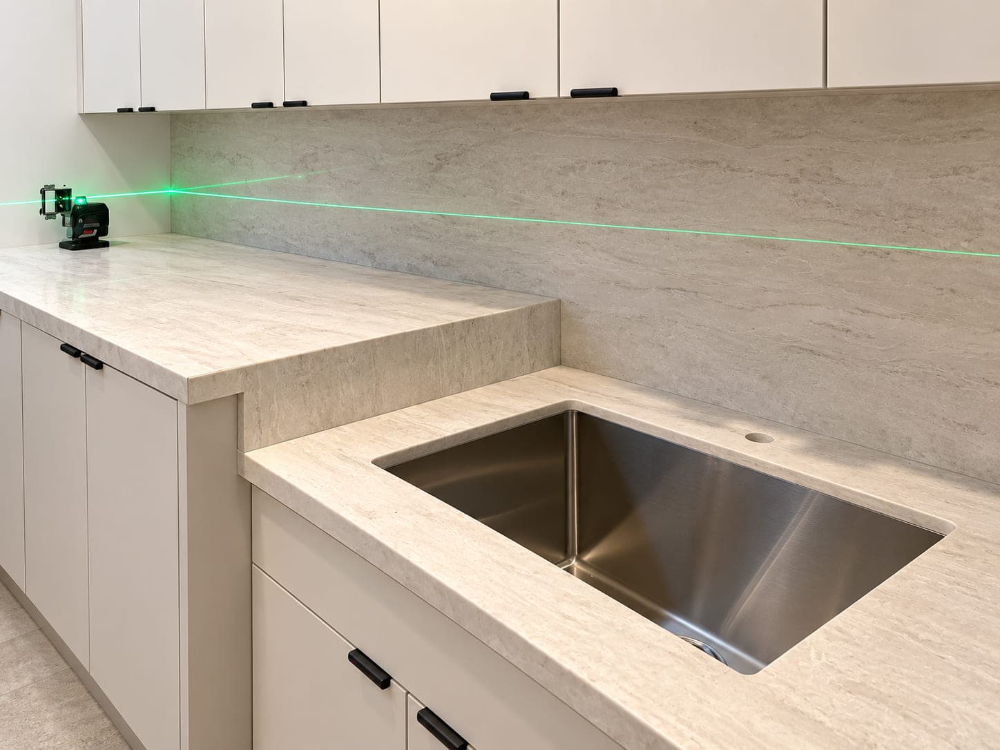 Green laser line across a pale stone kitchen backsplash and countertop