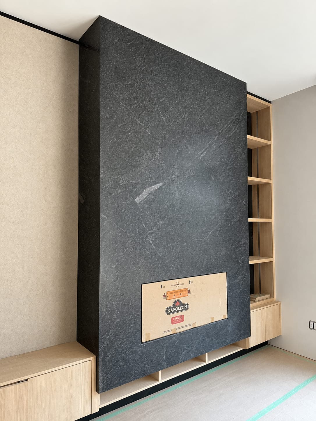 Full-slab dark stone fireplace wall mid-installation, with the fireplace insert still boxed in its shipping packaging