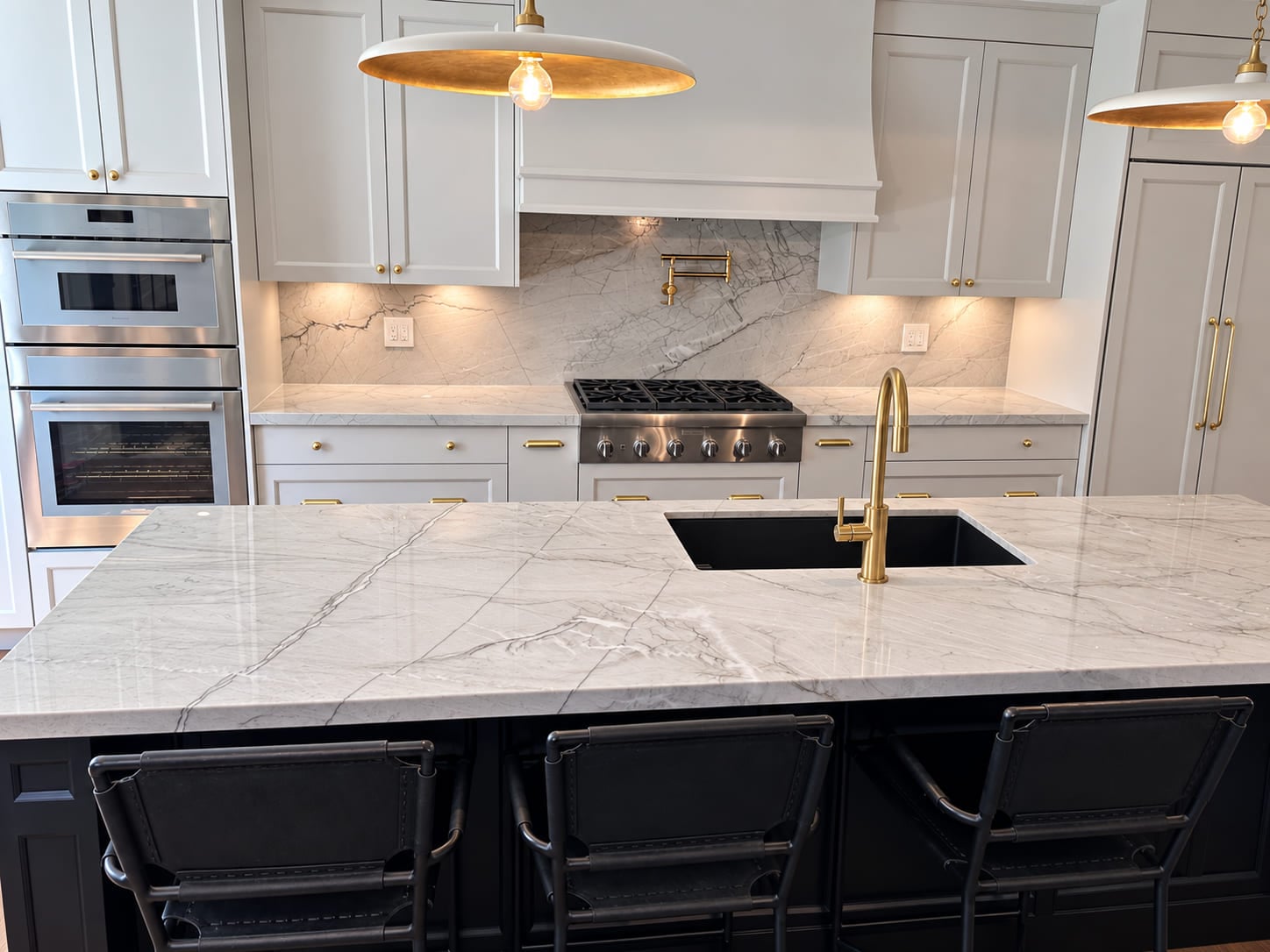White kitchen with a veined stone island, dark island cabinetry and brass lighting