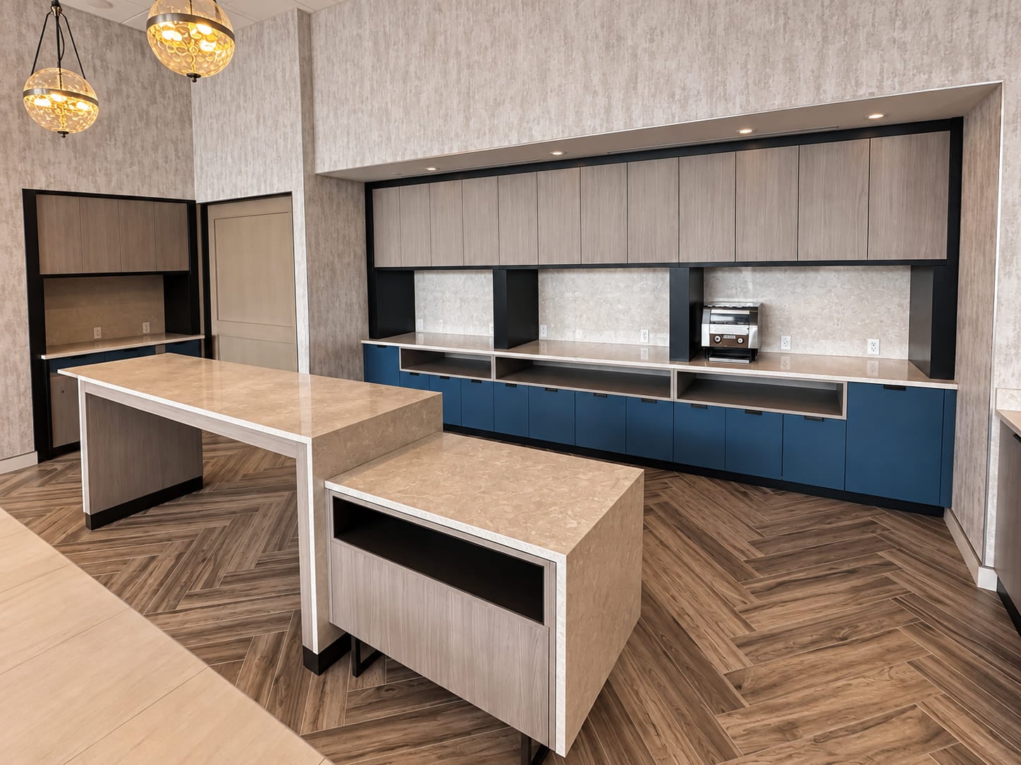 Pale stone waterfall island with blue cabinetry and pendant lighting