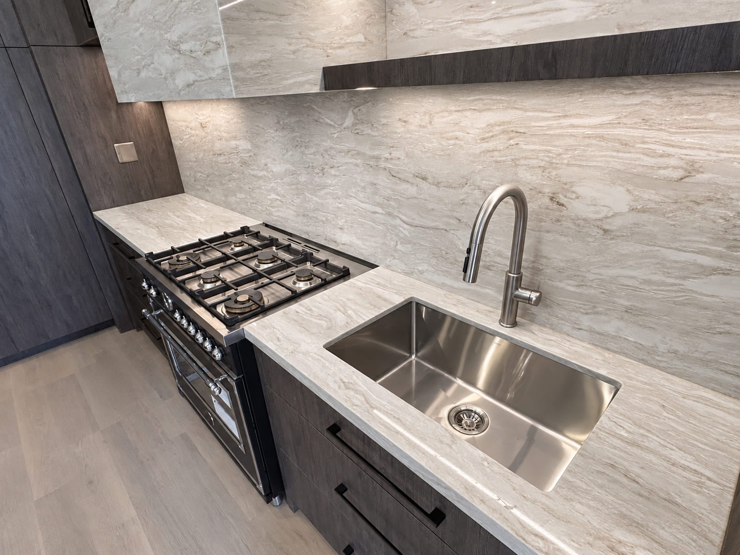 Range and undermount sink set into a pale stone counter below a full-height backsplash