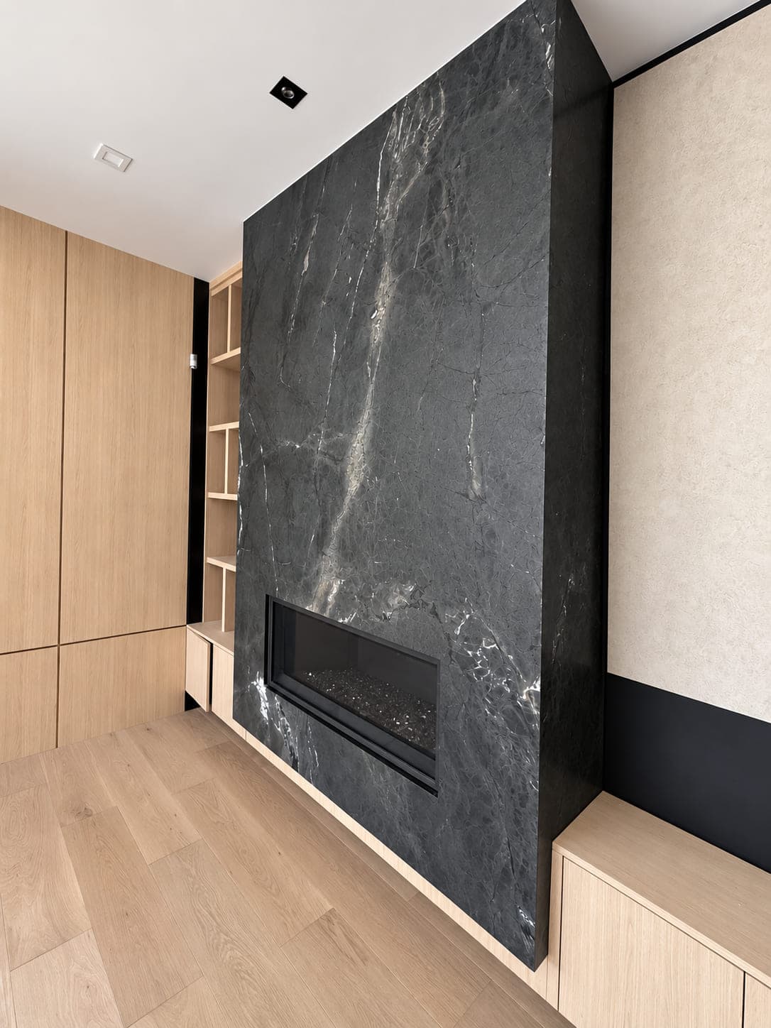 Dark veined stone fireplace wall framed by pale wood cabinetry