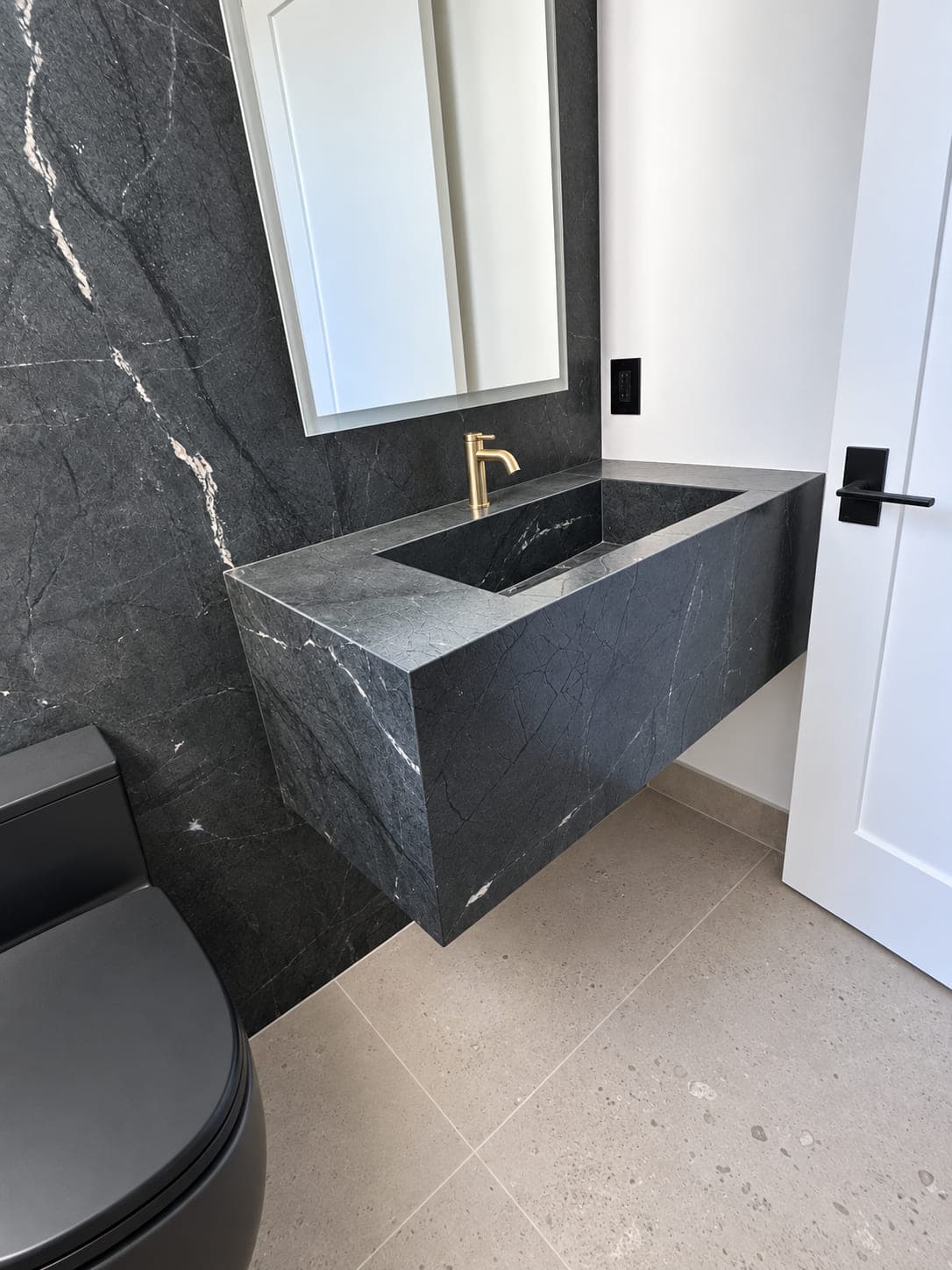 Dark stone floating vanity with an integrated basin and brass faucet