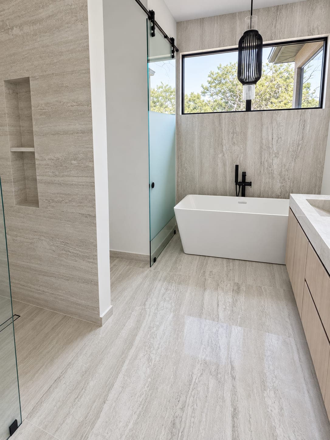 Freestanding bathtub beside a stone vanity with matching pale wall and floor surfaces