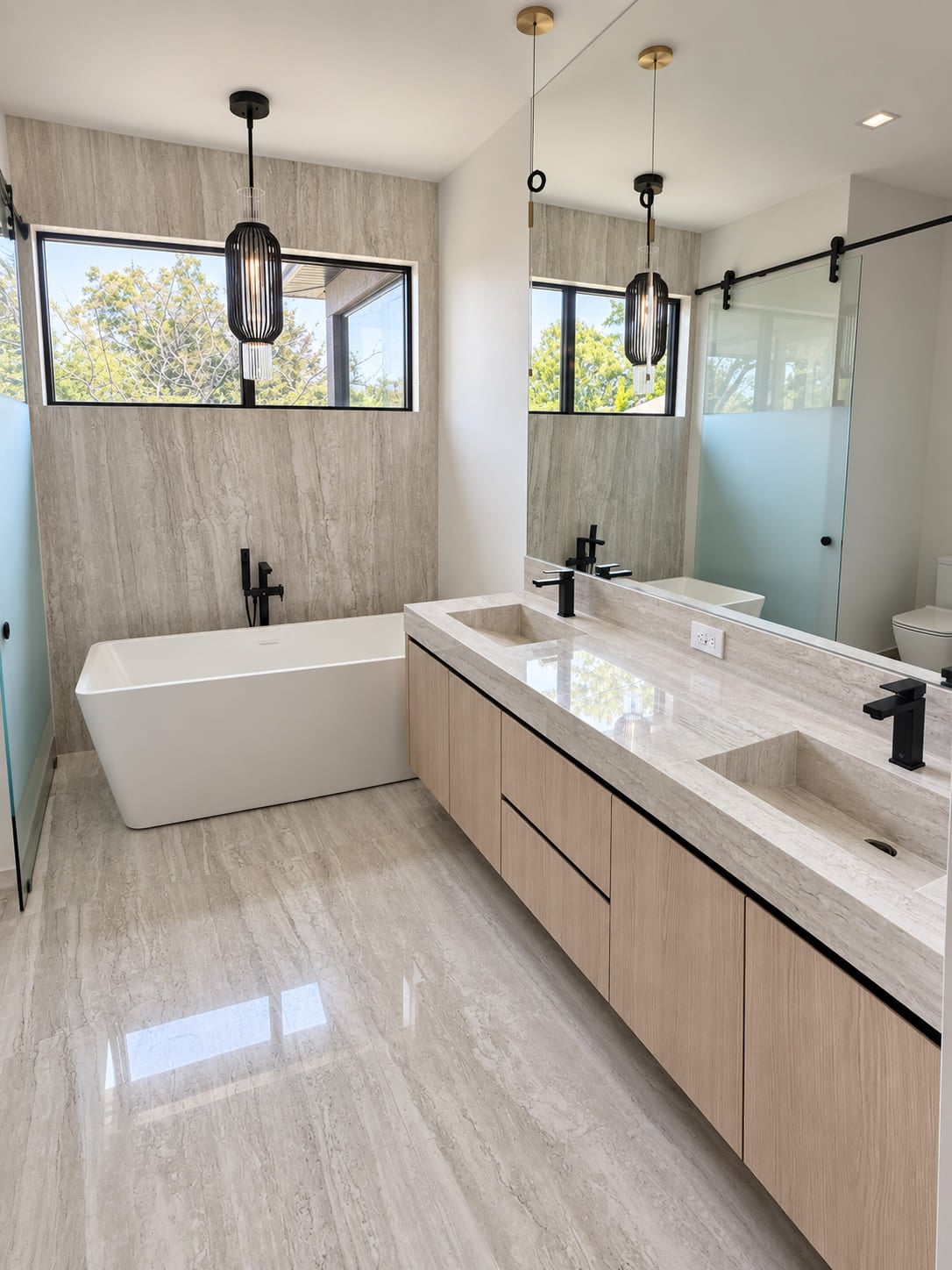 Pale stone double vanity with integrated basins, wood cabinetry and black fixtures